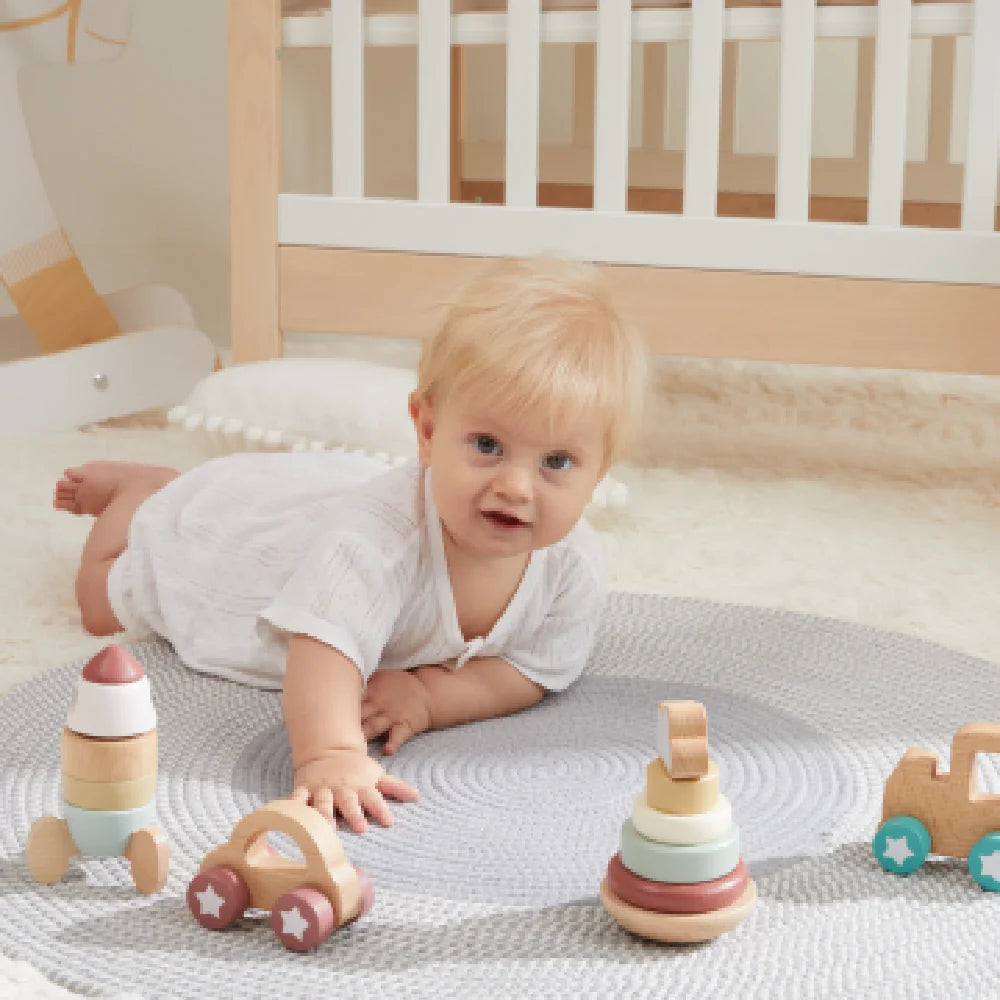 Baby playing with wooden educational toys on rug near crib.