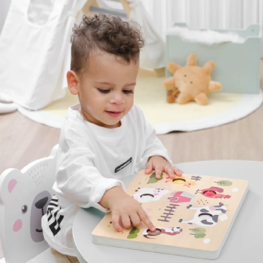 Toddler playing with wooden farm animal puzzle on a table.