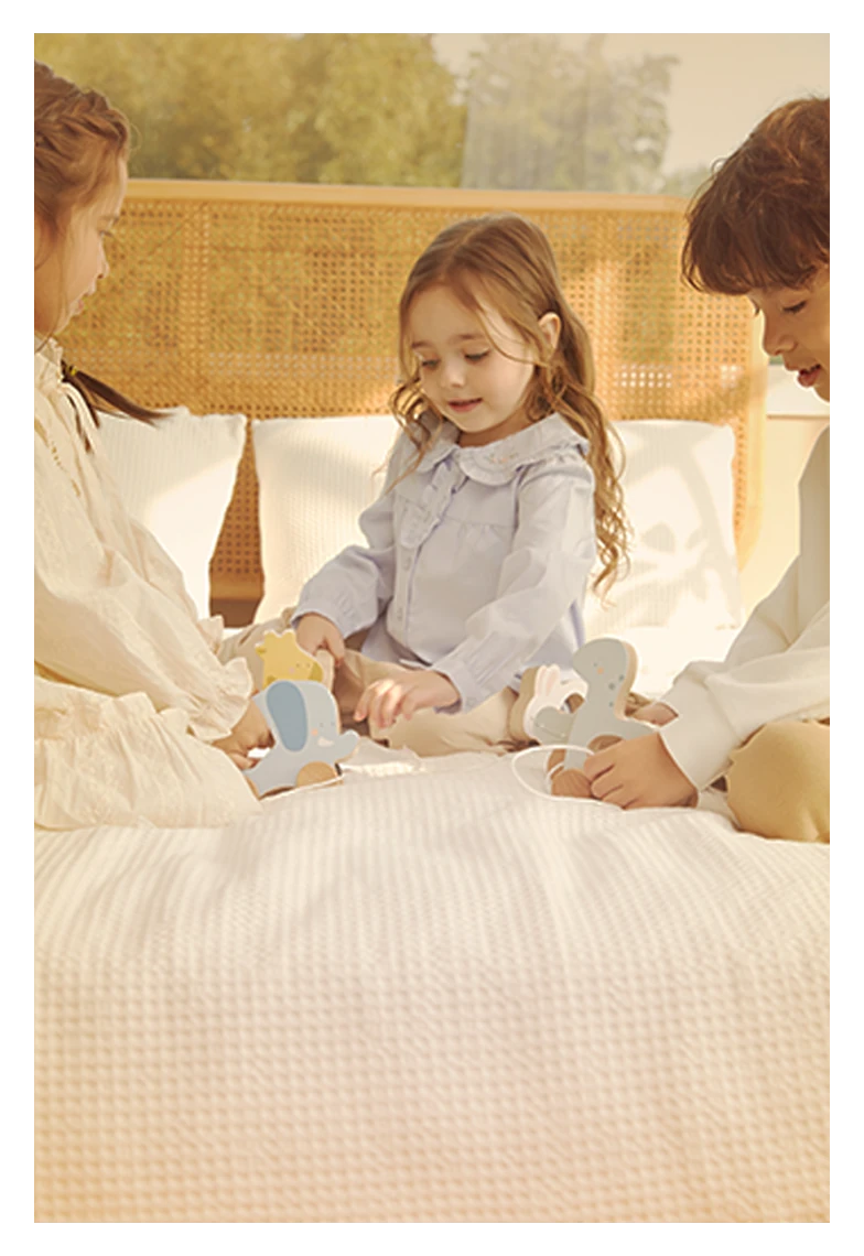 Child plays with wooden animal toys on a bed with two adults.