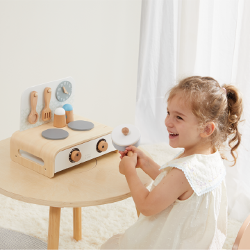 Young girl playing with wooden toy kitchen stove on small table