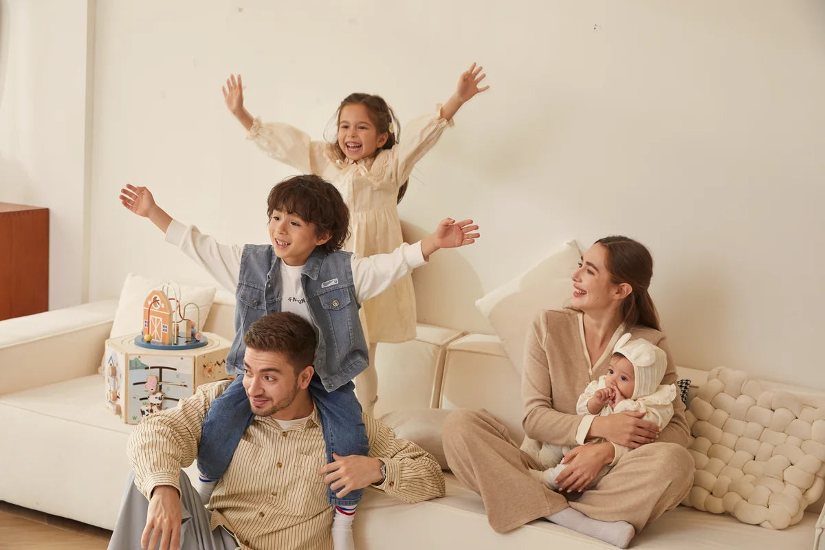 Family on white couch with wooden educational toy (barn) nearby.