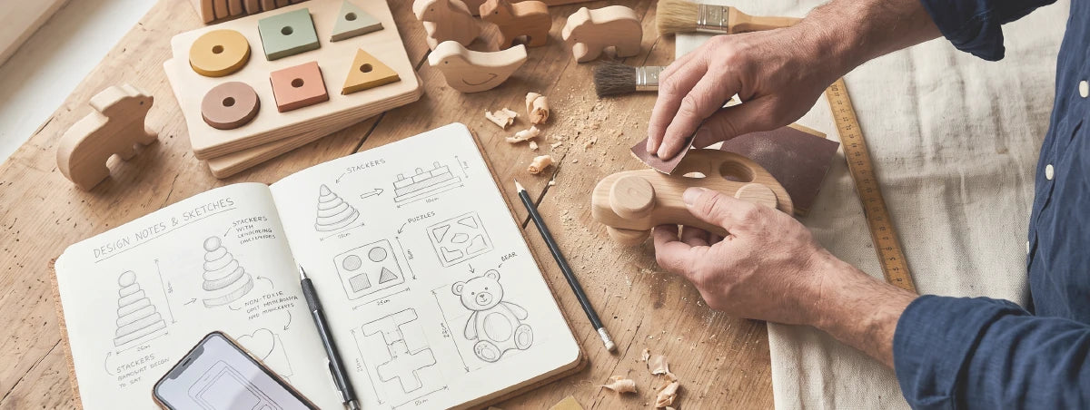 Craftsman sanding wooden toy near open design notebook and wooden educational toys