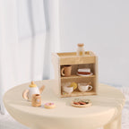 Wooden toy kitchen set with teapot, cups, cookies, and milk bottle on a table.