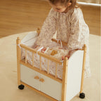 Little girl playing with a doll in a white wooden toy crib
