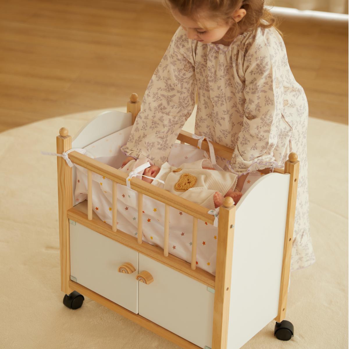 Little girl playing with a doll in a white wooden toy crib