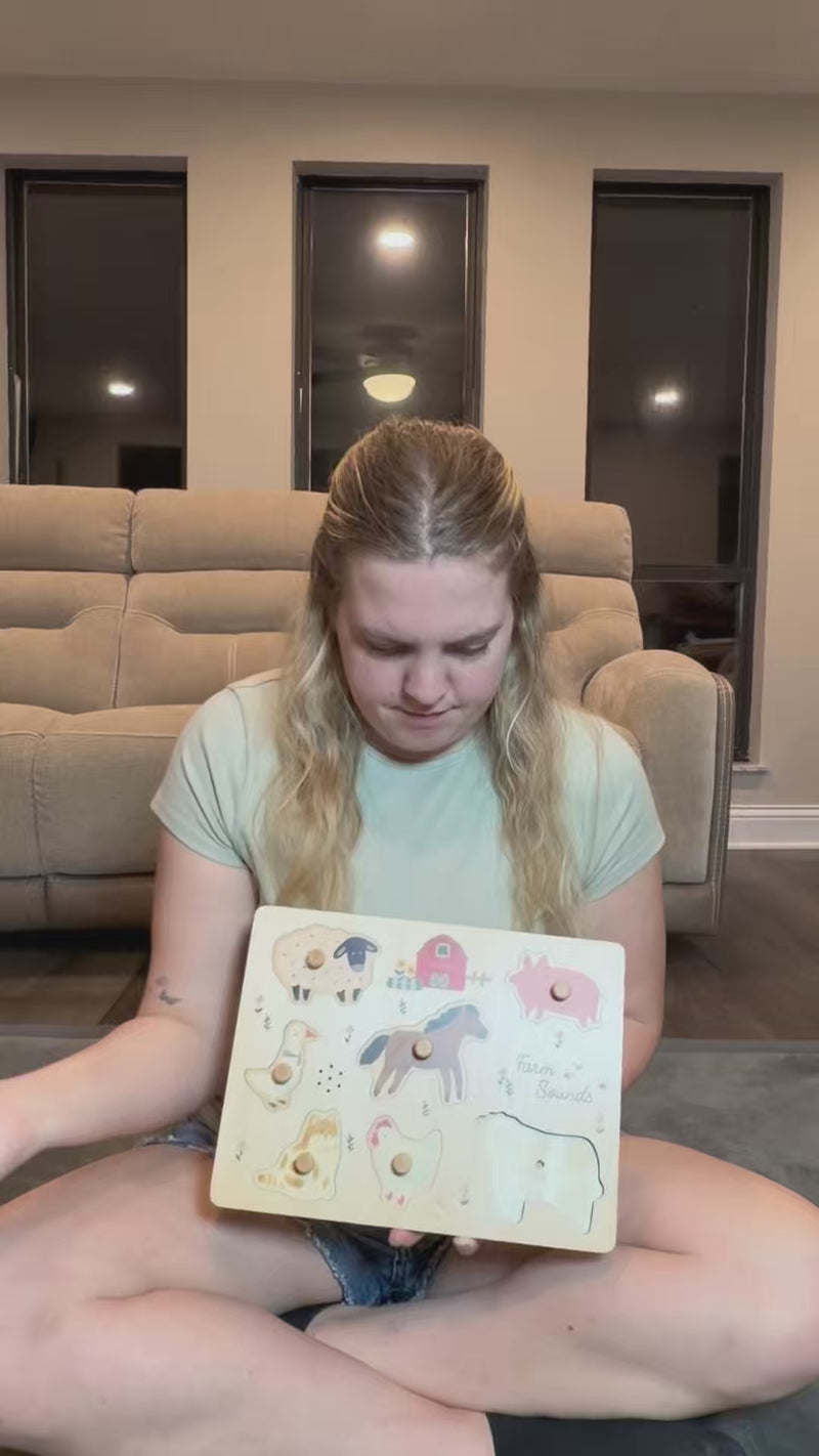 A woman sits cross-legged on the floor holding a wooden animal puzzle.; Woman showing wooden animal puzzle on floor.
